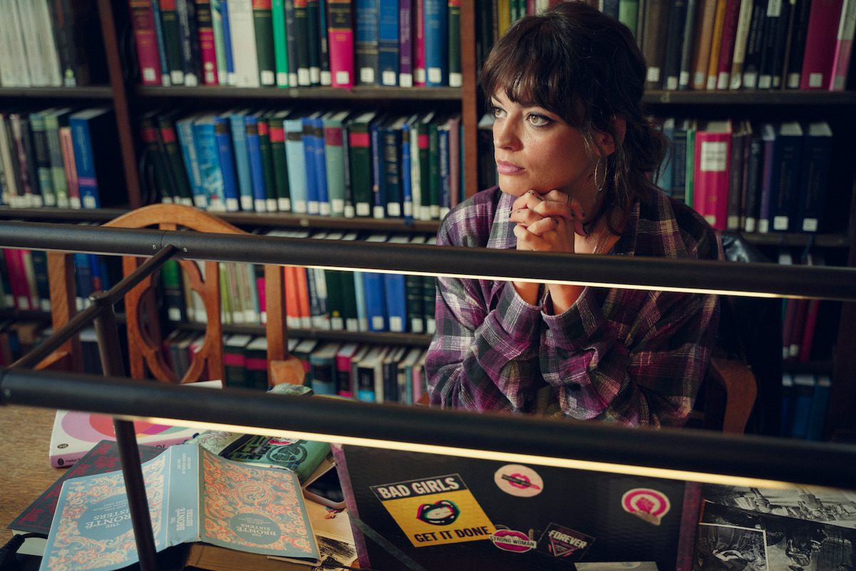 Emma Mackey as Maeve Wiley sits in a library with her hands folded in Season 4 of ‘Sex Education’