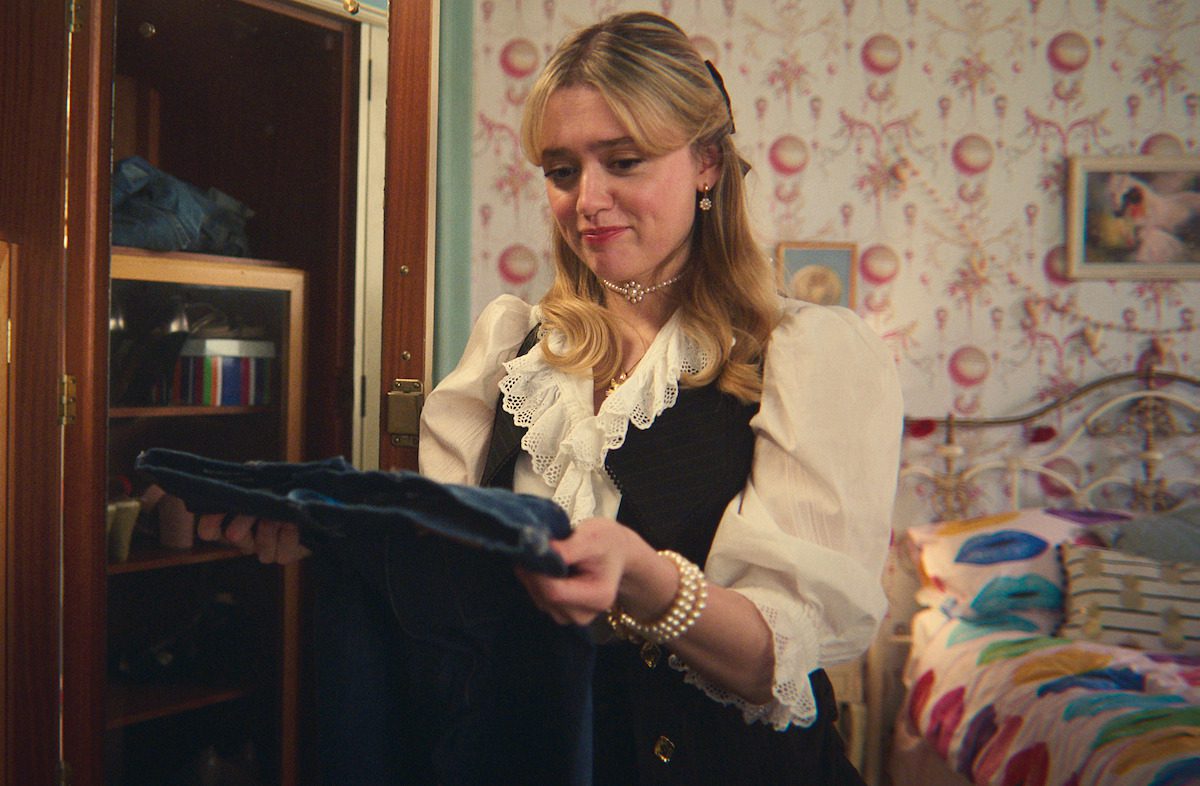 Aimee Lou Wood as Aimee holds a pair of jeans from her closet in Season 4 of ‘Sex Education’